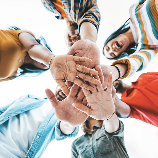 Group of happy and smiling people all putting their hands together to portray teamwork