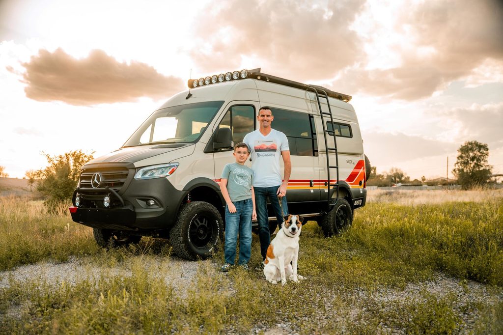Steve, Luke, and Pickles the dog standing in a field at sunset in front of a Storyteller Beast Mode Adventure Van