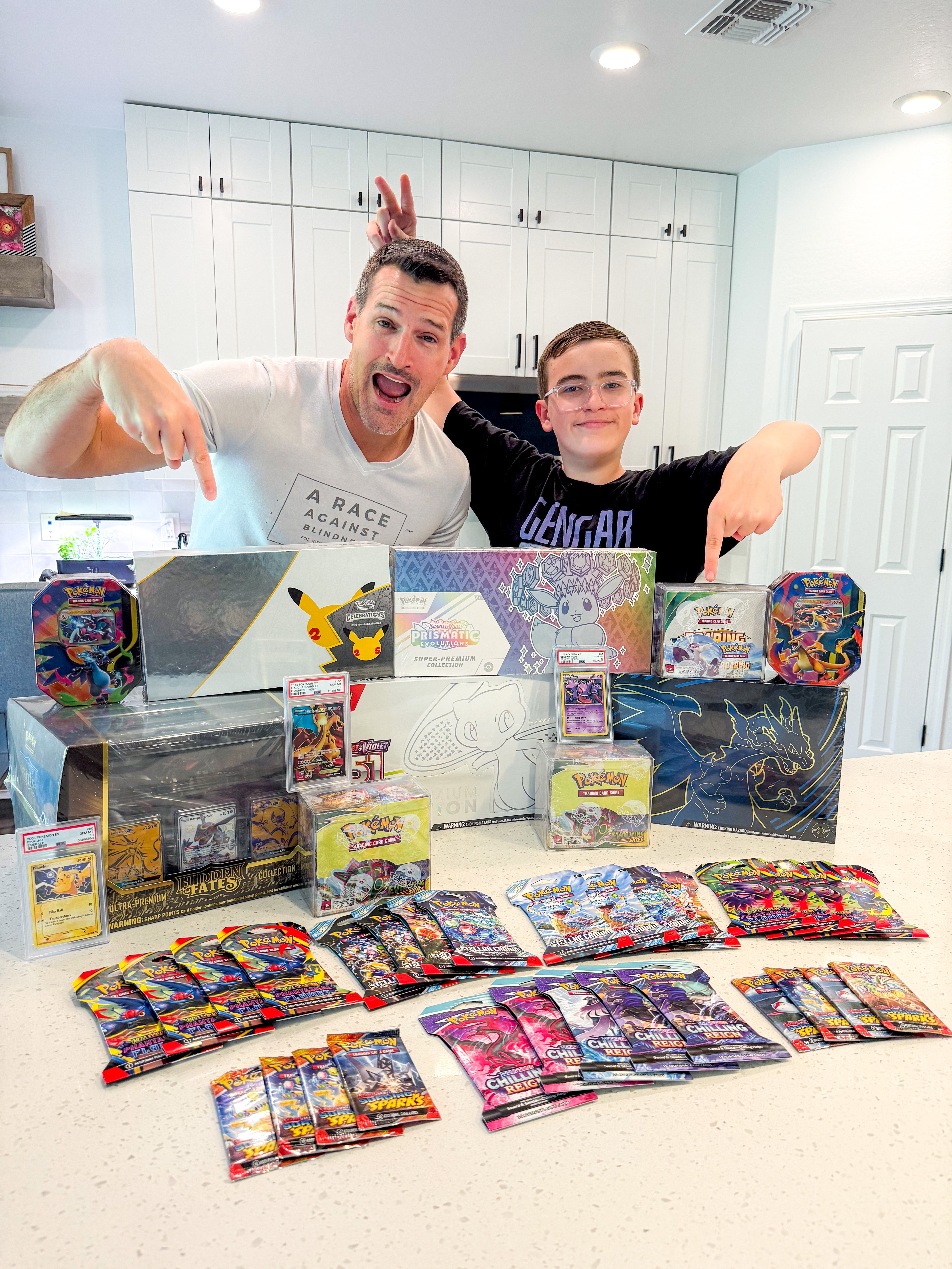 Two people with a collection of trading card packs on a kitchen counter.